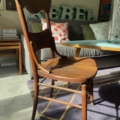 Dans une pièce ensoleillée, une Chaise de Bureau Américaine 1930 en bois complète le canapé, les coussins et la table basse posés sur un tapis à motifs. Brocante 93