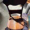 Une chaise en bois des années 1930 au dossier incurvé se prélasse au soleil sur un tapis violet et jaune, rappelant une Chaise de Bureau Américaine 1930, à côté du bord bleu de la table. Brocante 93