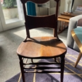 La Chaise de Bureau Américaine 1930, une chaise en bois au dossier incurvé, repose élégamment sur un tapis, baignée de lumière du soleil qui filtre à travers la fenêtre. Brocante 93