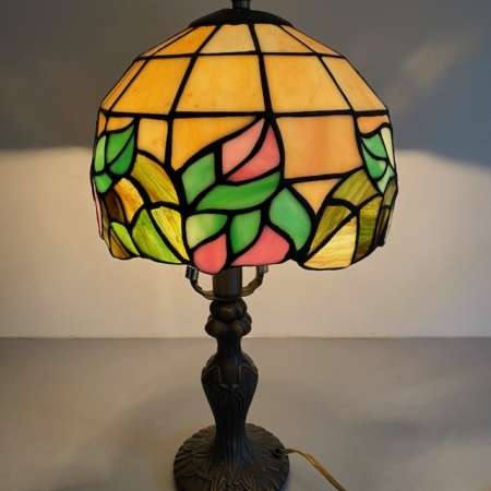 La lampe Tiffany avec vitrail présente des motifs floraux dans des tons de rose, de vert et de jaune sur une élégante base sombre. Brocante 93