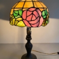 La Lampe Tiffany est dotée d'un superbe abat-jour en verre teinté avec un motif floral, mis en valeur par une rose rose saisissante. Brocante 93