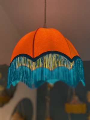 La Suspension Dome Velours, une superbe lampe suspendue orange ornée d'une finition velours et d'une frange bleue, est gracieusement suspendue au plafond, ajoutant du charme à la pièce. Brocante 93