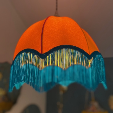 La Suspension Dome Velours, une superbe lampe suspendue orange ornée d'une finition velours et d'une frange bleue, est gracieusement suspendue au plafond, ajoutant du charme à la pièce. Brocante 93