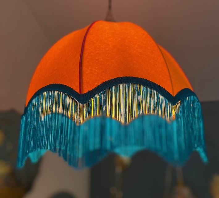 La Suspension Dome Velours, une superbe lampe suspendue orange ornée d'une finition velours et d'une frange bleue, est gracieusement suspendue au plafond, ajoutant du charme à la pièce. Brocante 93