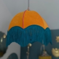 Voici la suspension Dome Velours, un abat-jour de style vintage confectionné en velours luxueux. Il arbore une ravissante teinte orange et est élégamment orné de franges bleu sarcelle, tombant gracieusement du plafond. Brocante 93