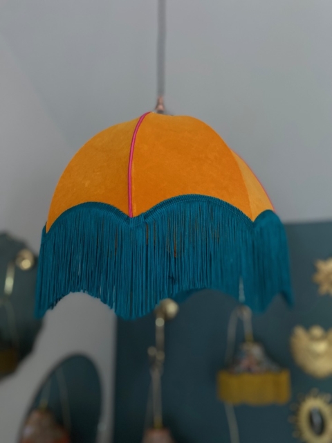 Voici la suspension Dome Velours, un abat-jour de style vintage confectionné en velours luxueux. Il arbore une ravissante teinte orange et est élégamment orné de franges bleu sarcelle, tombant gracieusement du plafond. Brocante 93