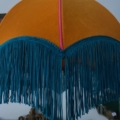 La suspension Dome Velours présente un abat-jour orange accueillant avec des accents de velours, élégamment complété par une frange bleue en cascade. Brocante 93