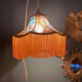 La Baladeuse Jaune est une lampe vintage ornée d'un motif floral coloré et d'une frange orange, projetant une lueur jaune chaleureuse. Brocante 93