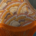 Gros plan de la Baladeuse Graphique, dotée d'un abat-jour recouvert d'un tissu coloré à motifs en éventail et agrémenté de franges orange vibrantes. Brocante 93