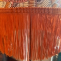 Gros plan de la Lampe Abat-Jour Eventail, présentant un motif de plumes vibrant et une frange orange saisissante. Brocante 93