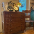 La Commode Grise 1950, ornée d'une lampe et d'un vase en verre, fait écho à son charme rustique à côté d'une chaise en bois dans une pièce cosy. Brocante 93