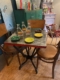 Découvrez le charme d'un Bistrot de Table des années 50 avec son ambiance café vintage cosy, avec table en métal, chaises en bois, assiettes colorées et bouteilles exposées. Brocante 93