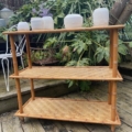 L'Étagère Bambou 1960 se dresse élégamment sur la terrasse en bois, mettant en valeur des plantes en pot prospérant sous le ciel ouvert, encadrées par une verdure luxuriante. Brocante 93