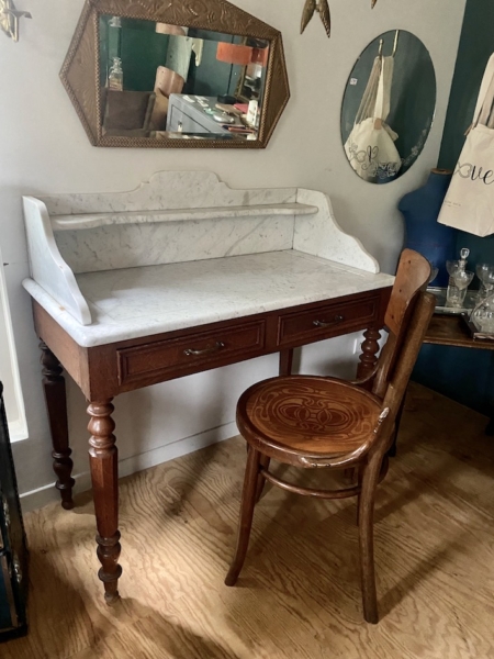 Bureau vintage élégant ressemblant à une Coiffeuse double des années 1940, doté d'un plateau en marbre et associé à une chaise en bois ornée dans une pièce chaleureuse et décorée. Brocante 93