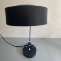 La Lampe Administrative 1960, lampe de bureau moderne noire, reprend le design épuré des années 60 avec sa base circulaire et son large abat-jour. Posée sur un fond clair, elle incarne une élégance intemporelle. Brocante 93